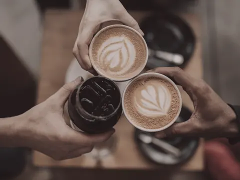 Drei Hände stoßen über einem Holztisch mit Kaffee an